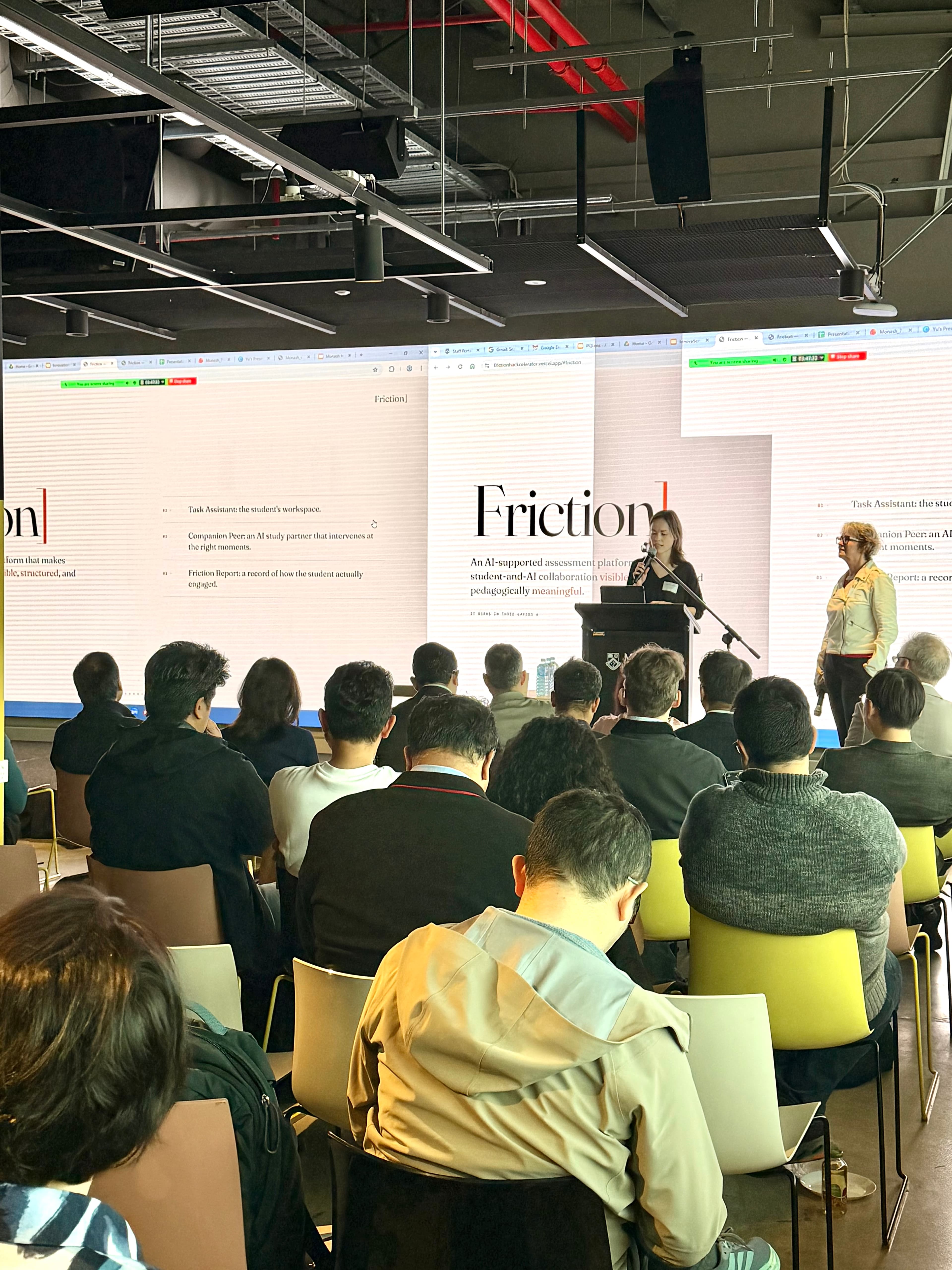 Dora Velenczei presenting Friction on stage at the Monash Innovation Summit, with the live prototype projected behind her.